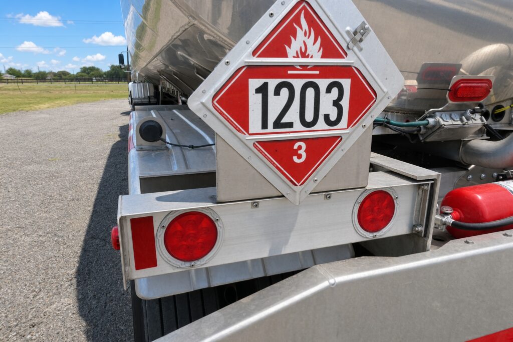 Hazard placard marked "1203" on the rear of a tanker truck, indicating the transport of flammable material. Reflective lights and safety features visible.